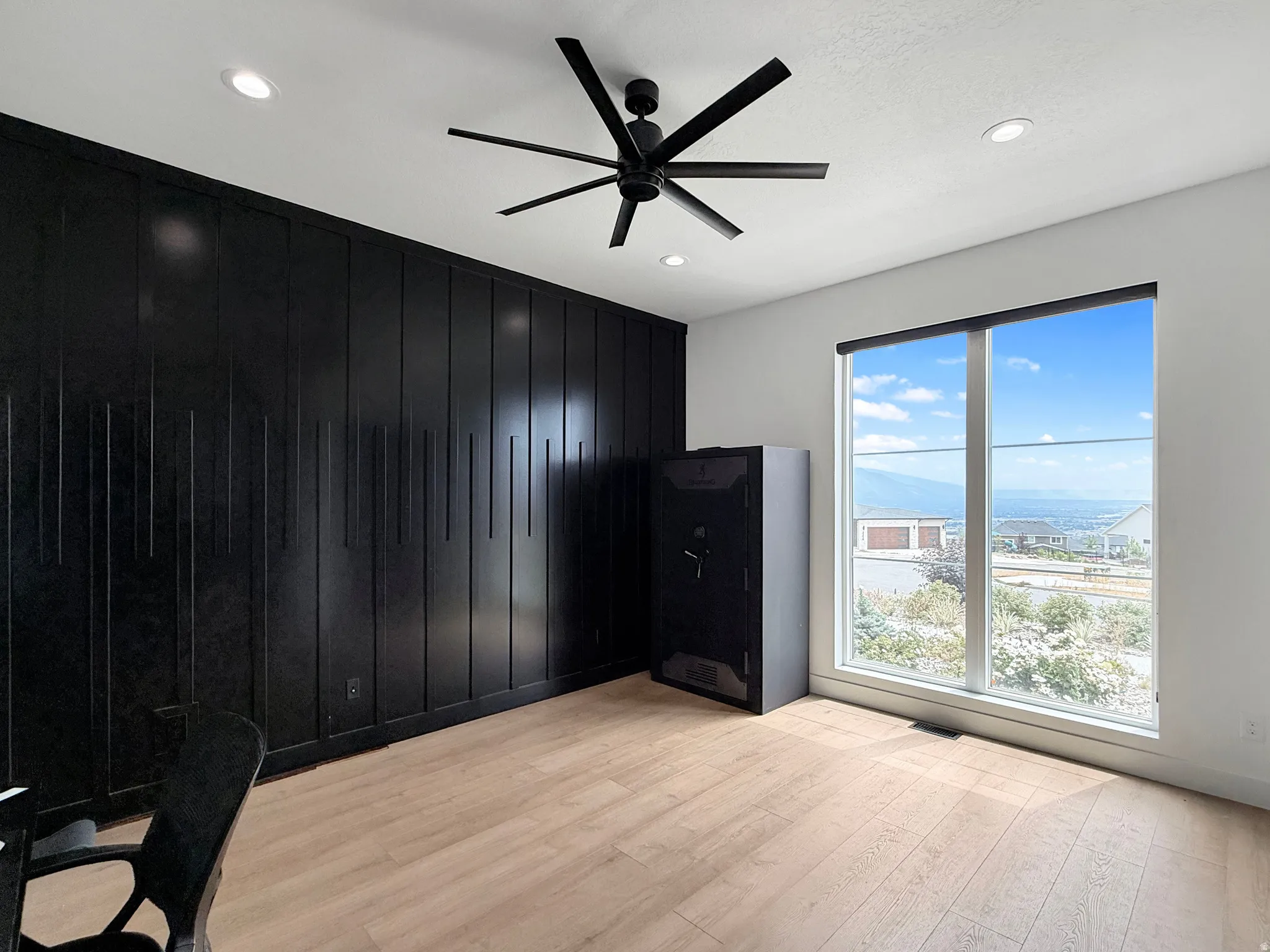 Black accent wall with vertical paneling, light wood-finish flooring, recessed lighting, and a contemporary ceiling fan