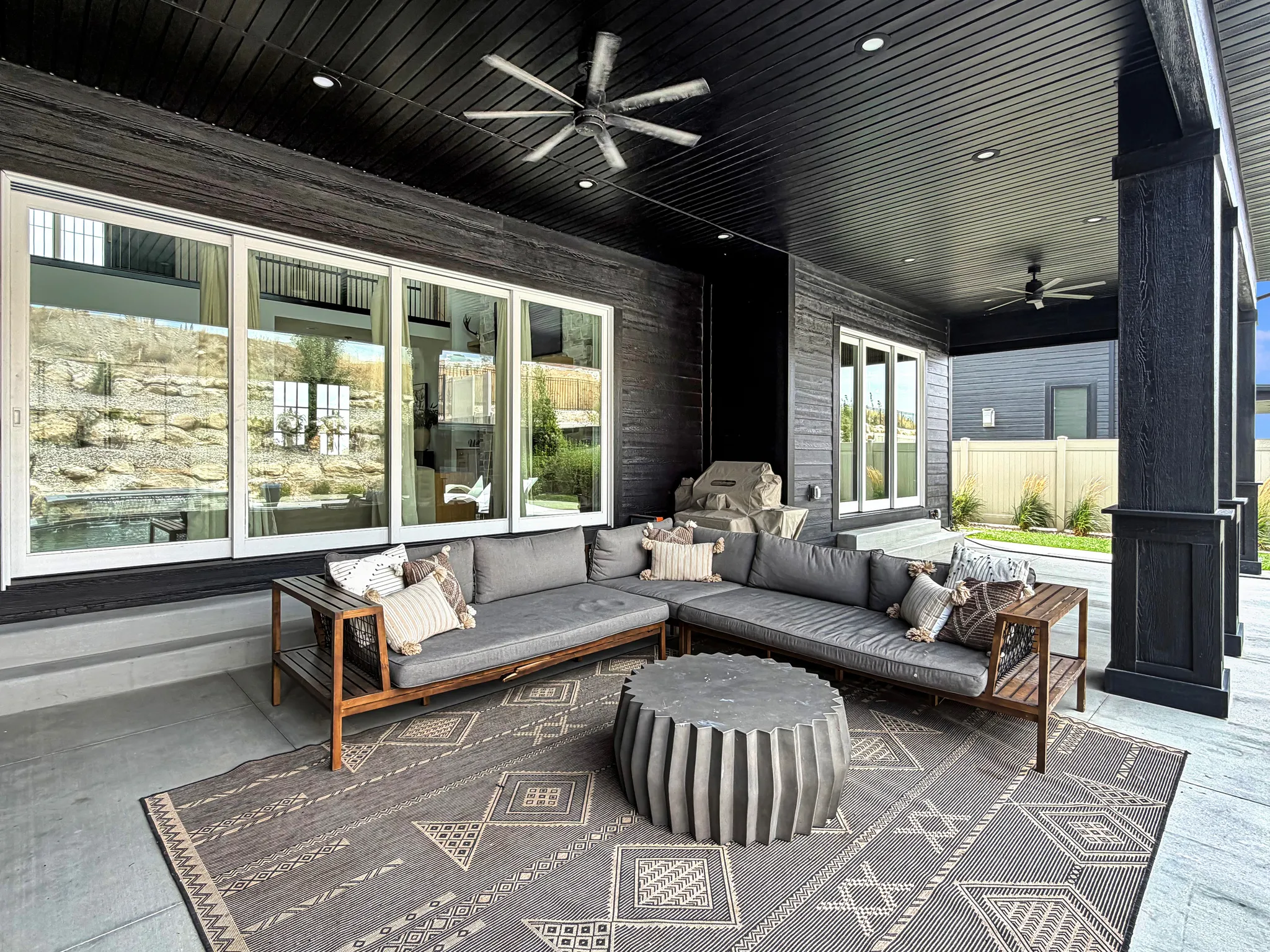 Expansive covered patio featuring a dark wood-paneled ceiling, recessed lighting, two ceiling fans, and large sliding glass doors