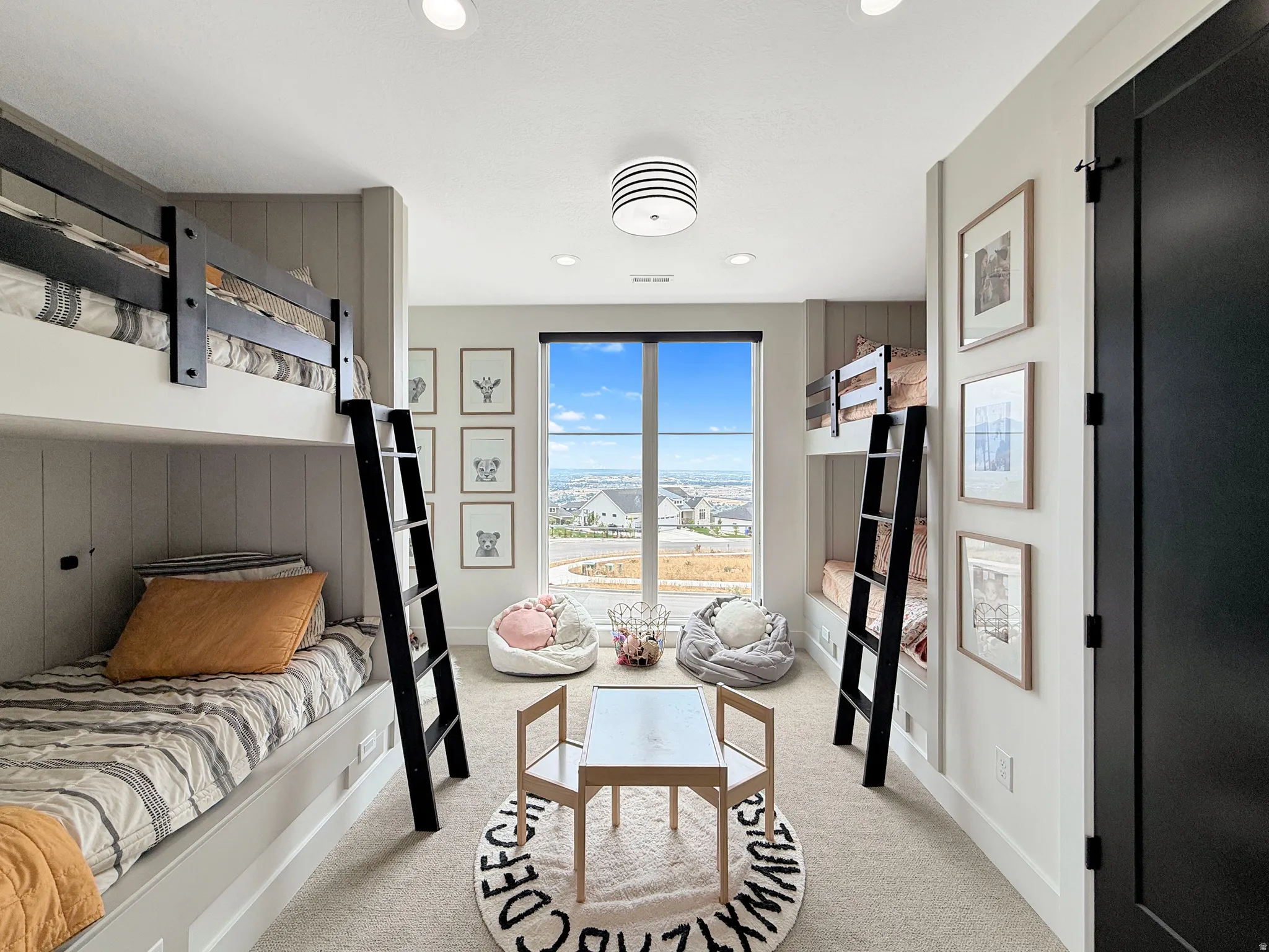 Built-in bunk beds with integrated ladders, recessed ceiling lighting, a large window, light-toned carpet, and a black interior door