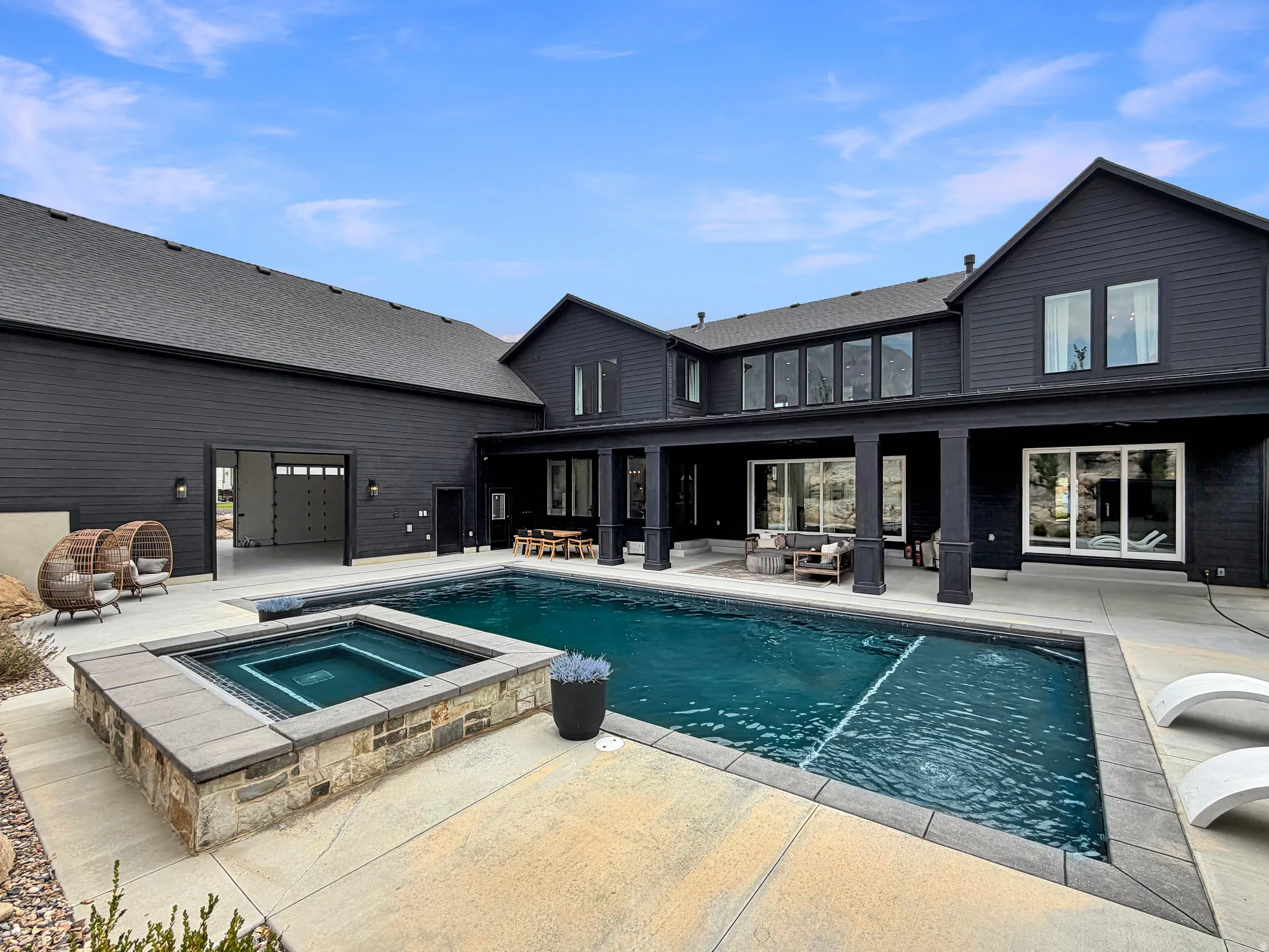 Expansive outdoor living area featuring a rectangular swimming pool, integrated spa with stone and block surround, and a covered patio