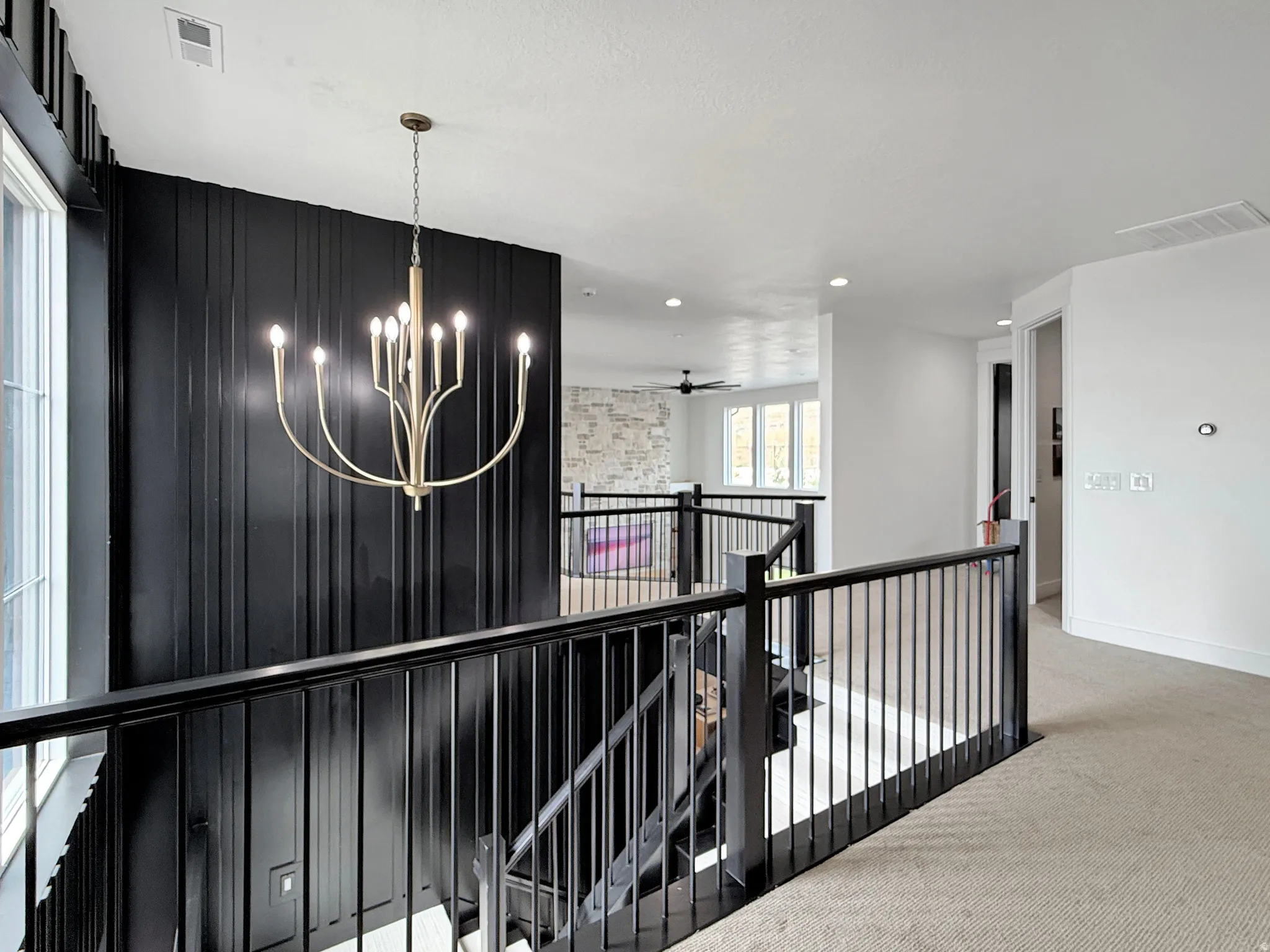 Black vertical panel accent wall, bronze-tone chandelier, black metal balusters, light-toned carpeting, and recessed ceiling lighting