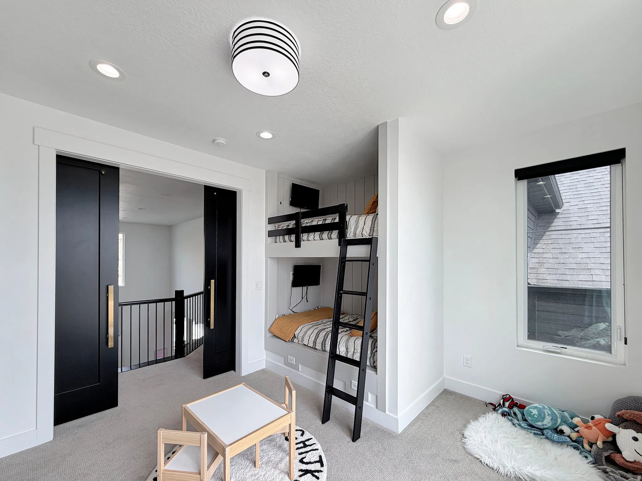 Built-in bunk beds, recessed lighting, sleek black sliding barn doors with gold-tone hardware, and a single pane window with a dark roller shade