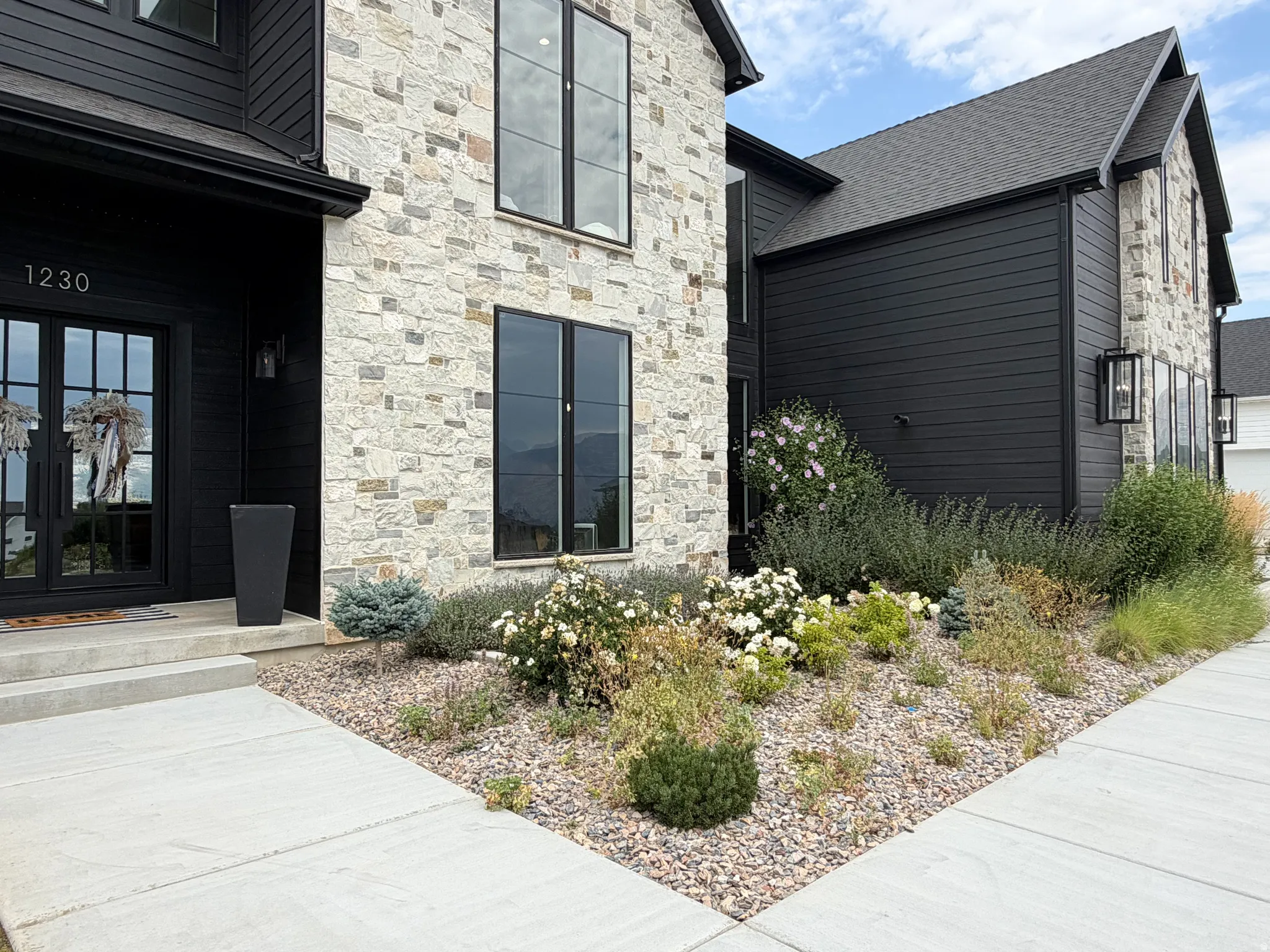 Stone and horizontal siding exterior with a dark-toned finish, featuring a prominent front entry with double glass doors, a landscaped rock garden, and dark-framed windows