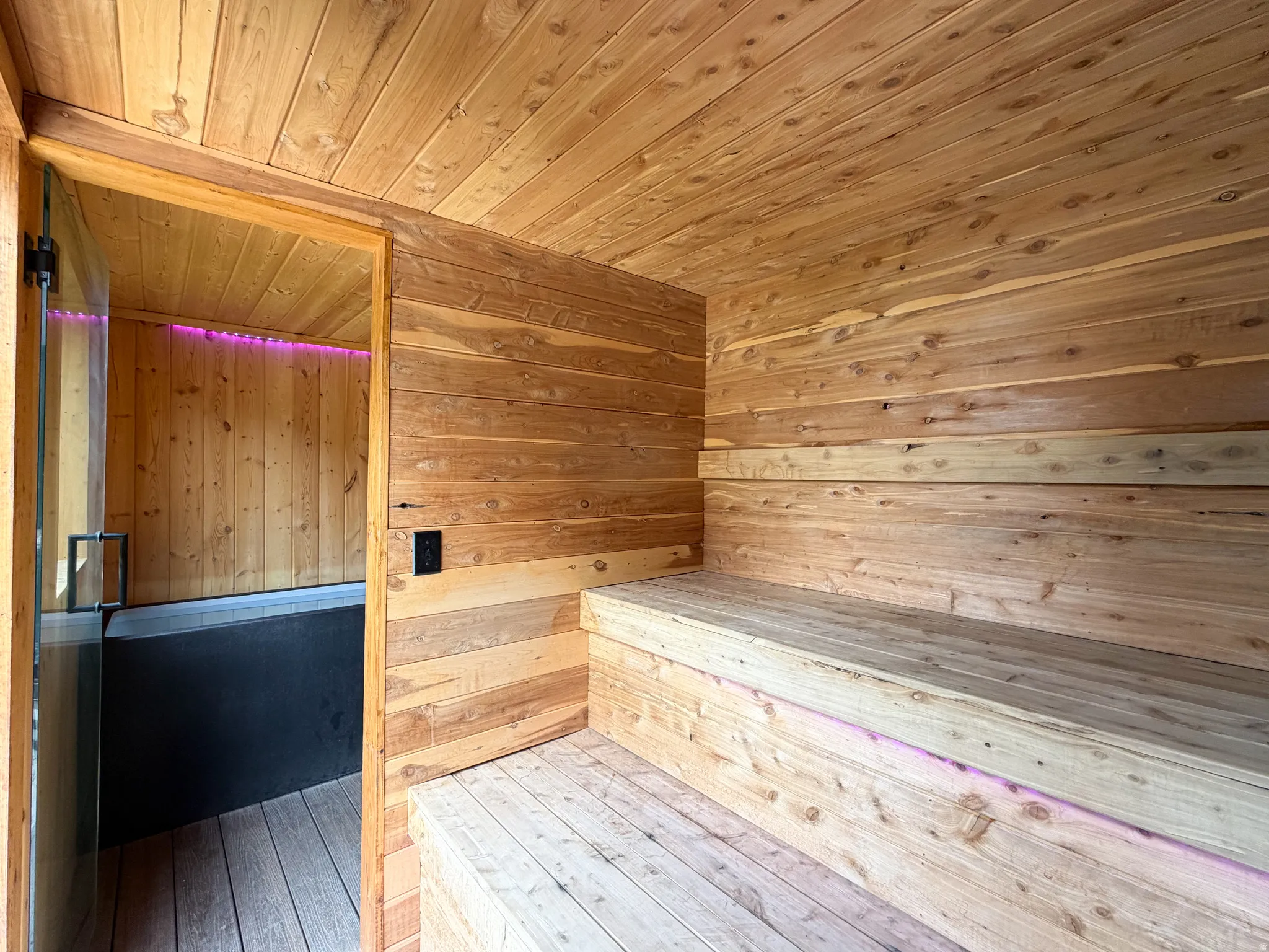 Wood-paneled interior featuring built-in wooden benches and an adjoining room with a dark-toned tub