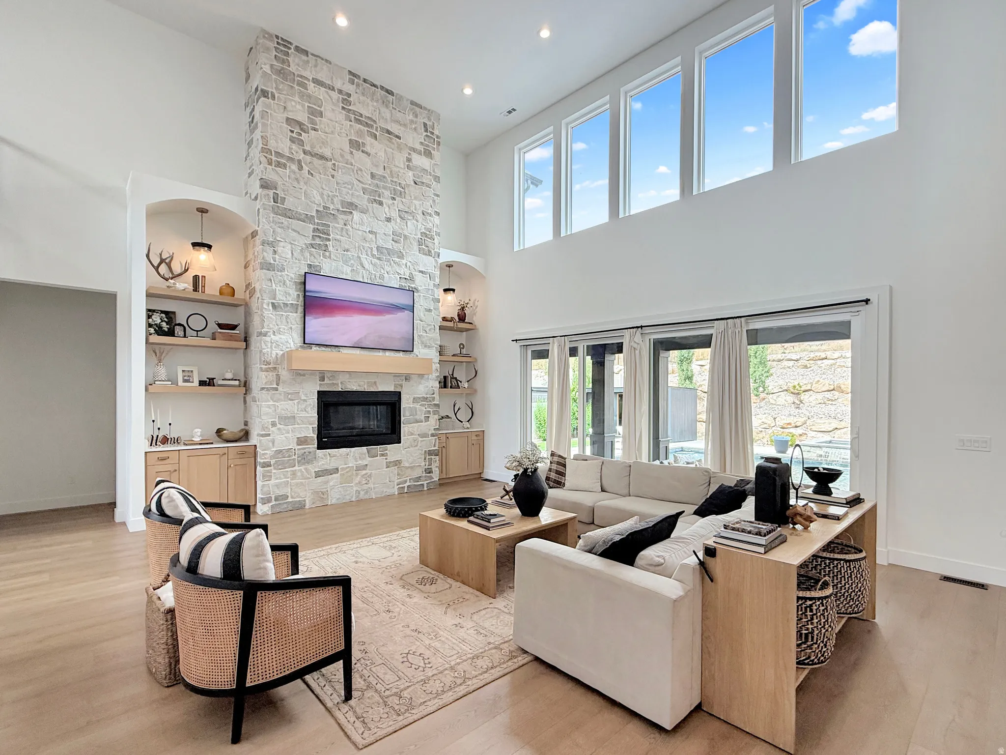 Vaulted ceiling living area featuring a stone fireplace, built-in shelving, wood-finish flooring, and upper transom windows