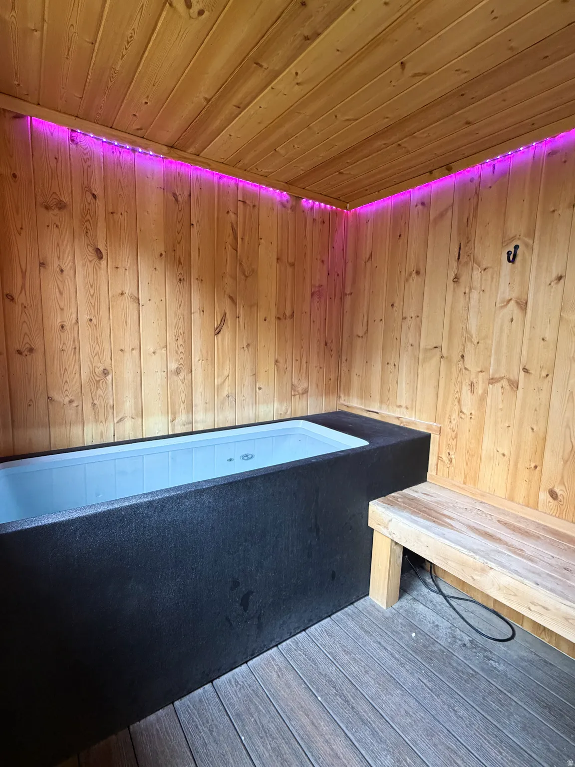 Wood-paneled walls and ceiling, built-in soaking tub, built-in wooden bench, and composite wood flooring