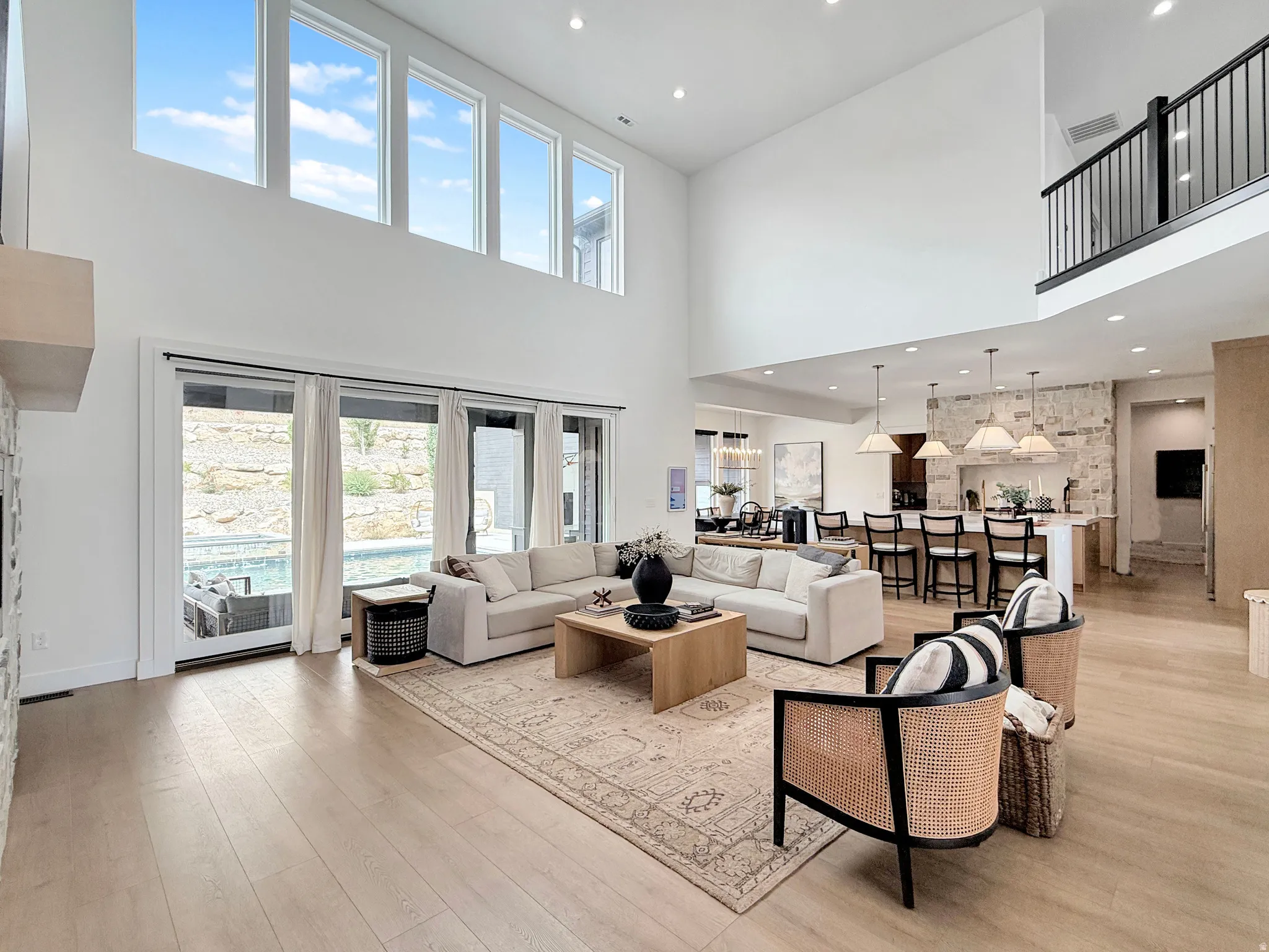 Double-height living area with wood-finish flooring, full-height windows, and a black metal railing