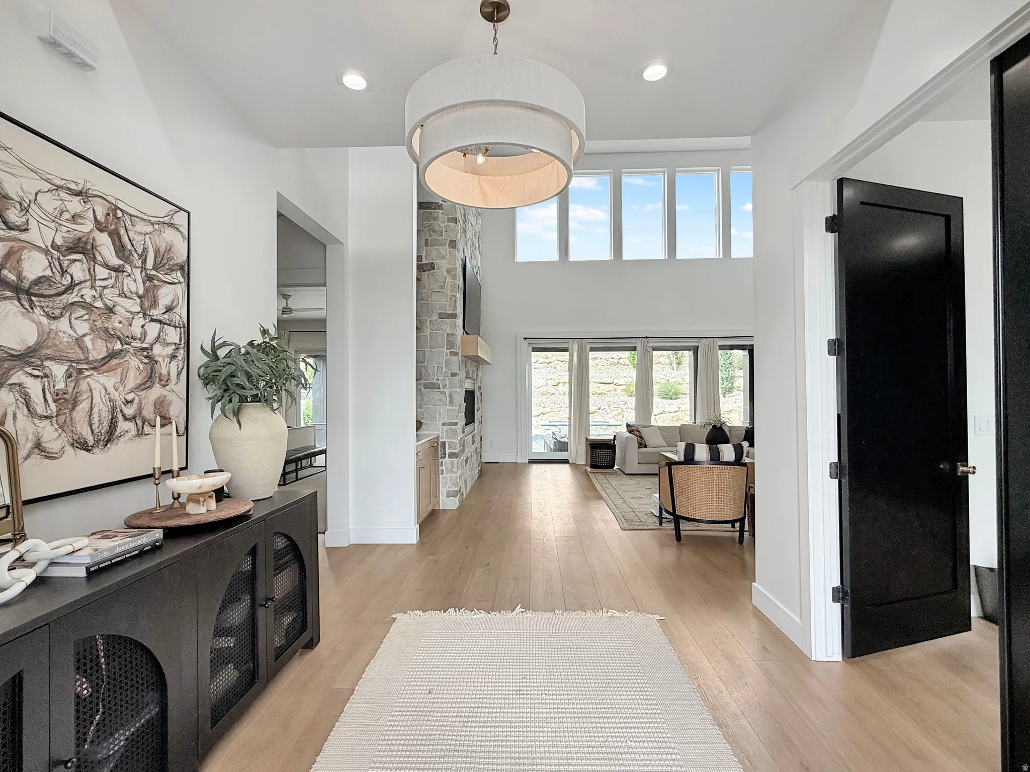 Two-story entryway with wood-finish flooring, a contemporary chandelier, a stone-clad fireplace, and abundant natural light from upper-level windows