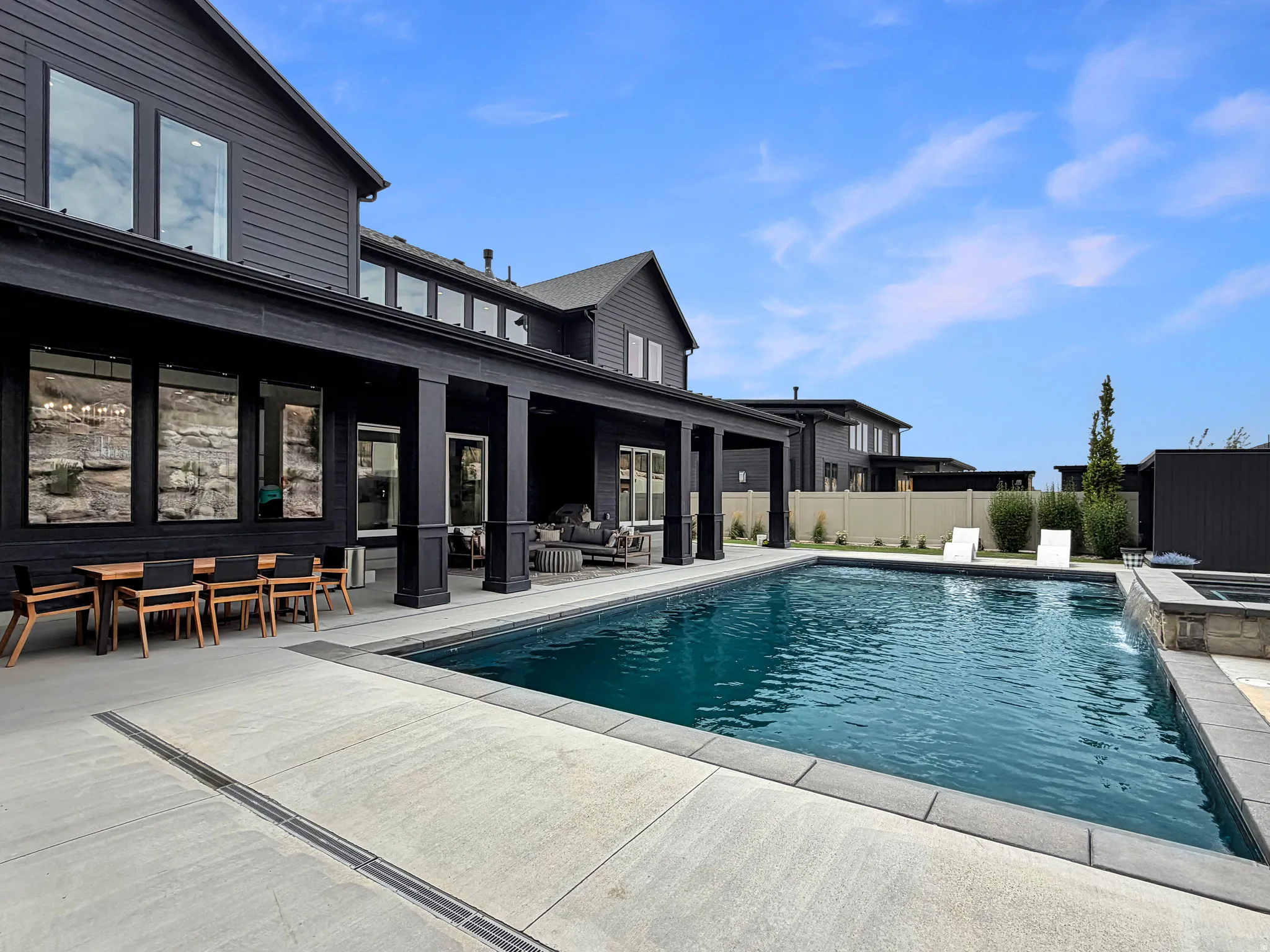 Expansive outdoor space featuring a rectangular swimming pool, stone-clad spa with a water feature, and a large covered patio with columns