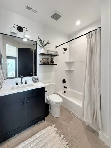 Modern bathroom featuring a black vanity with a white countertop and integrated sink, a full-size tub with a shower fixture, and light-toned patterned tile flooring