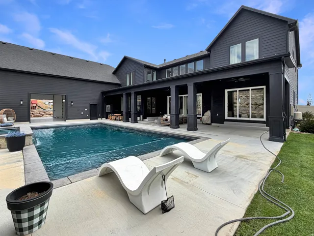 Expansive outdoor concrete patio featuring a built-in swimming pool and integrated hot tub, with a covered outdoor living area