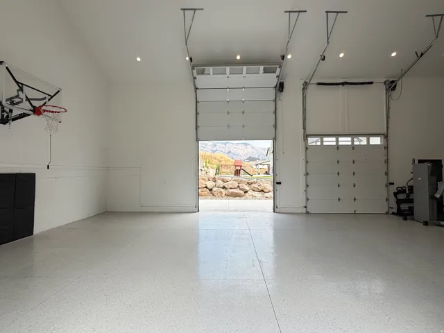 High-gloss epoxy flooring, multiple overhead garage doors, vaulted ceiling, recessed lighting, and white paneled walls