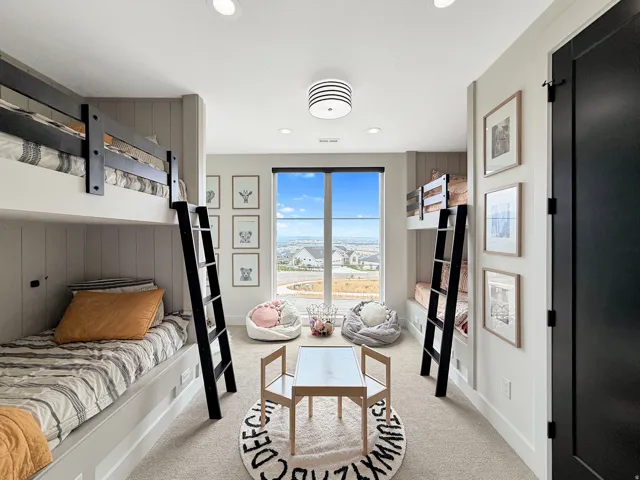 Built-in bunk beds with integrated ladders, recessed ceiling lighting, a large window, light-toned carpet, and a black interior door
