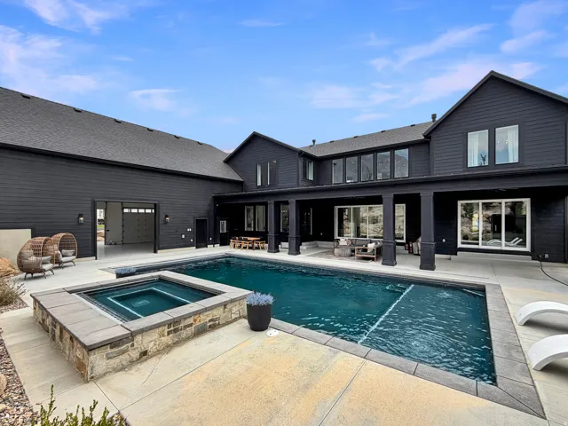 Expansive outdoor living area featuring a rectangular swimming pool, integrated spa with stone and block surround, and a covered patio