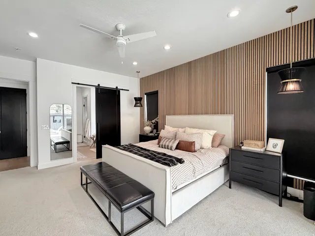 Wall-mounted wood paneling detail, recessed ceiling lights, ceiling fan, dark-finish barn door, and a dark-finish single-panel door