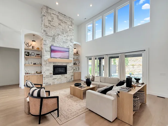 Vaulted ceiling living area featuring a stone fireplace, built-in shelving, wood-finish flooring, and upper transom windows