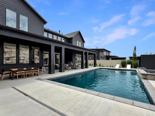 Expansive outdoor space featuring a rectangular swimming pool, stone-clad spa with a water feature, and a large covered patio with columns