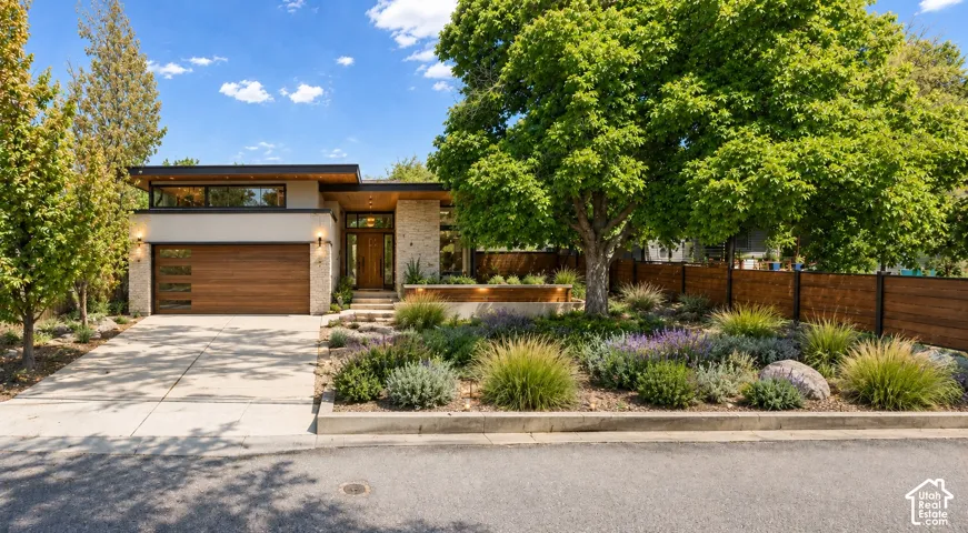 Modern exterior with stone accents, a wood-finish garage door, prominent front landscaping, and a wood privacy fence