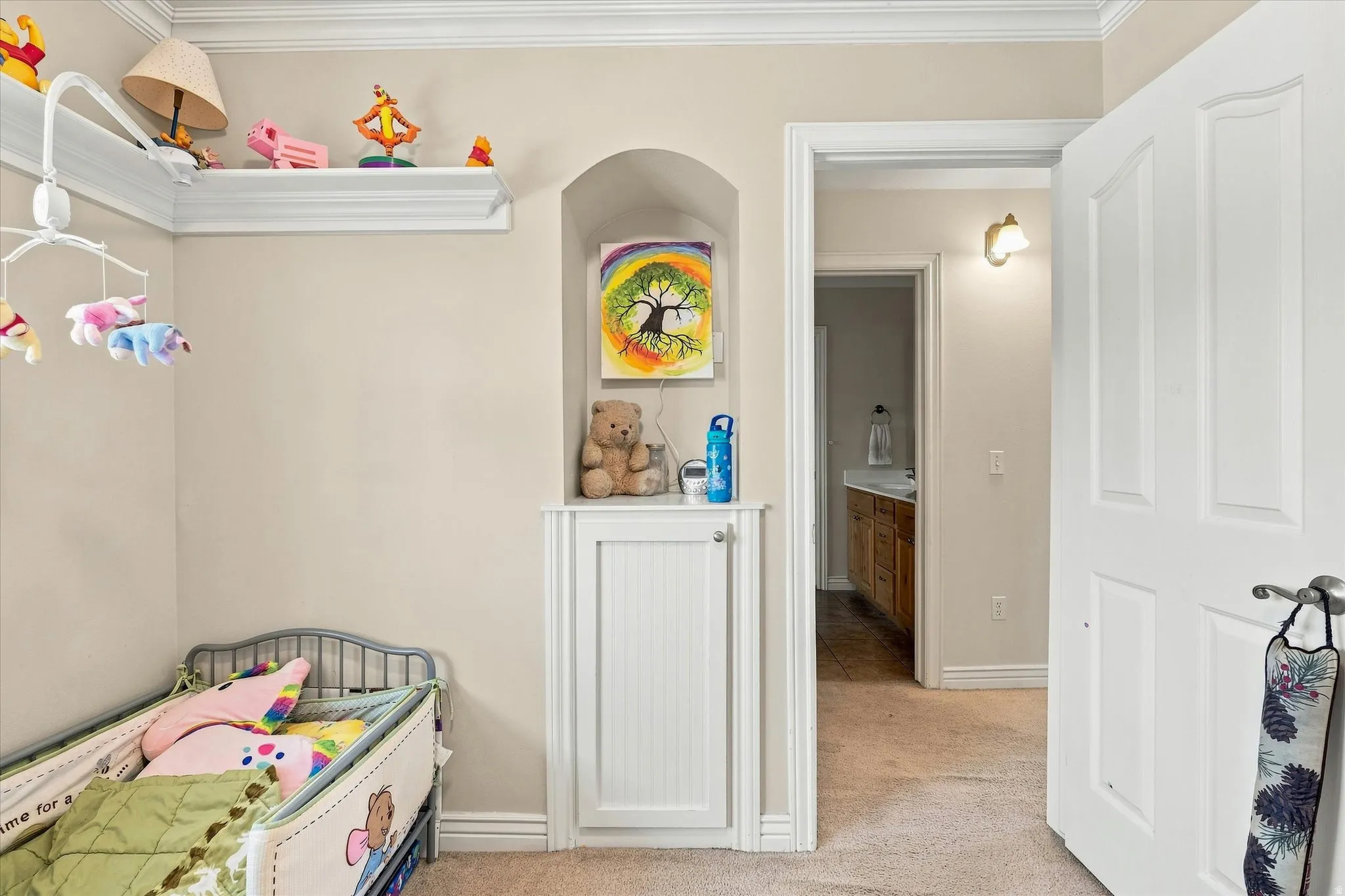 Built-in wall niche with beadboard cabinetry, crown molding, and an interior doorway leading to a bathroom with a wood-finish vanity