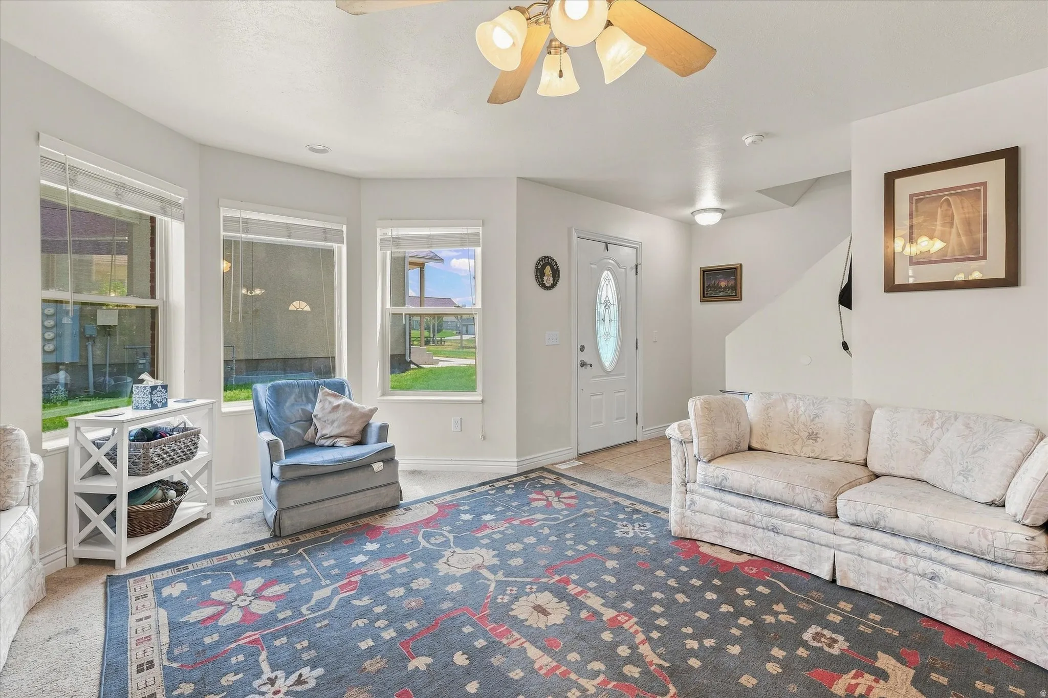Bright living area featuring a bay window, ceiling fan, and staircase access