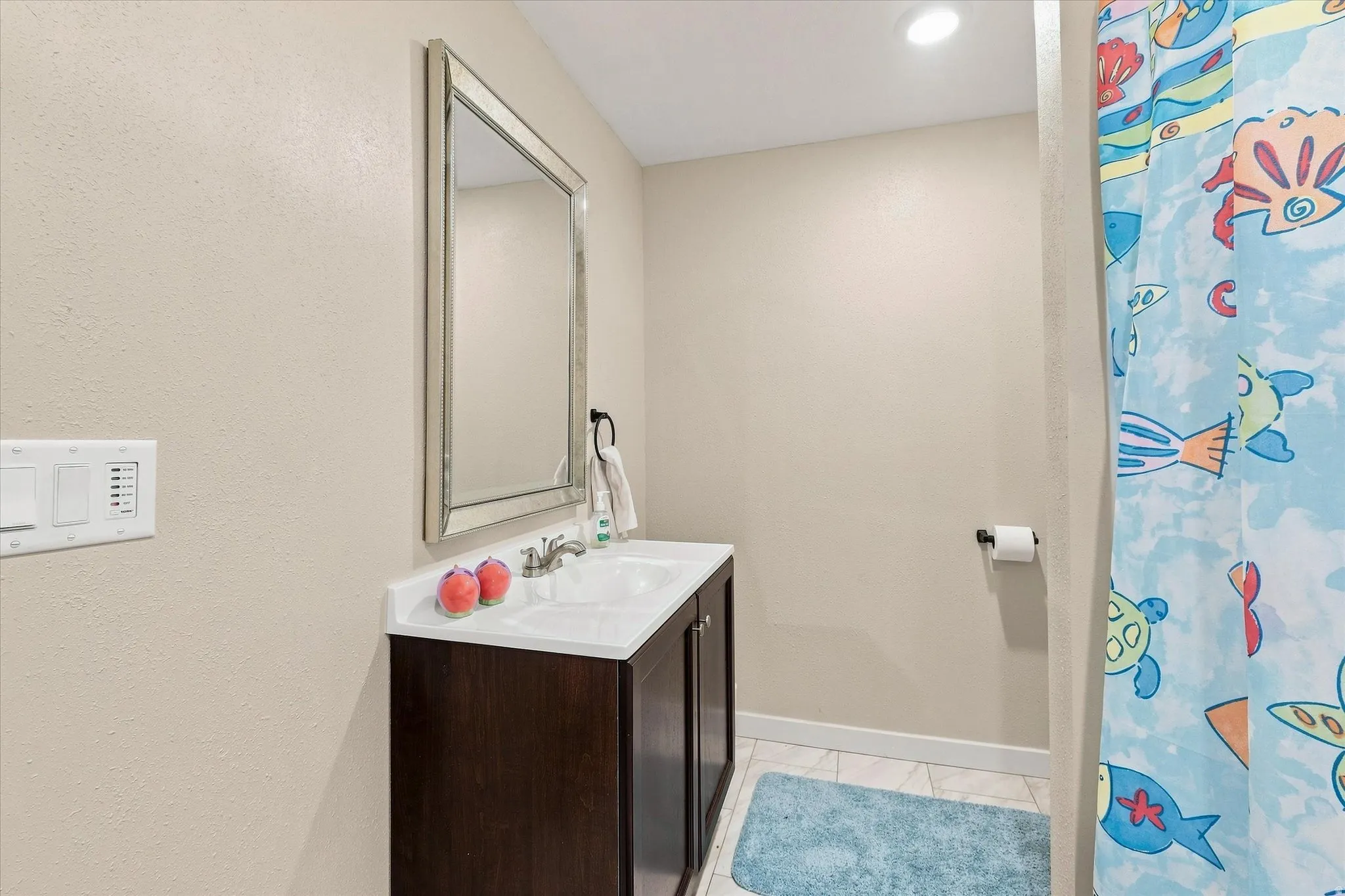 Recessed lighting, wood-finish vanity with a white countertop and integrated sink, framed mirror, and tile flooring