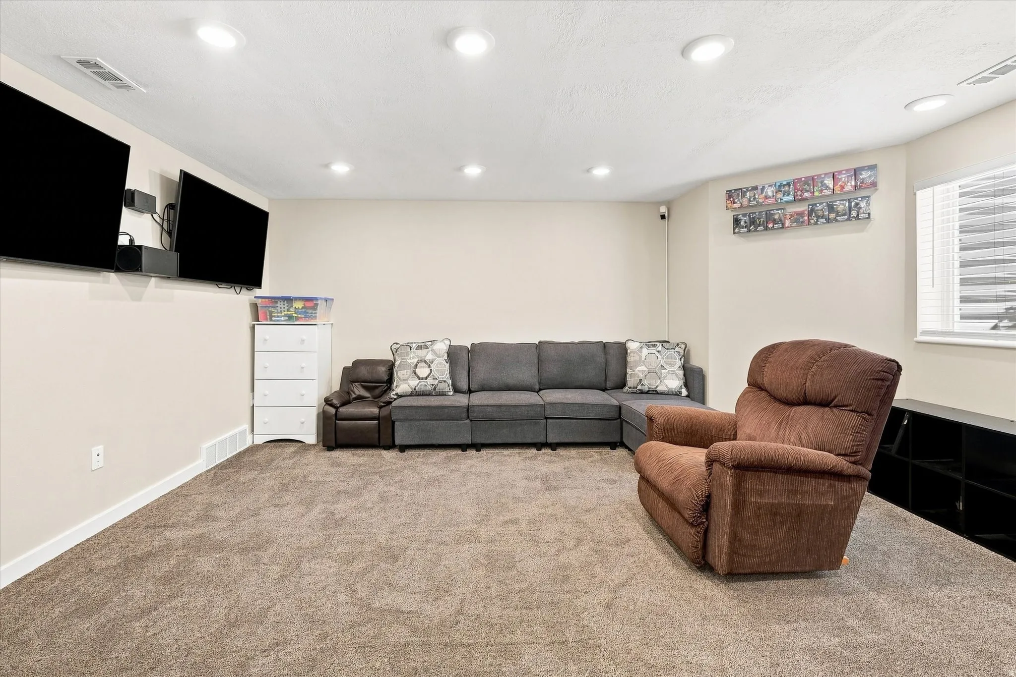 Recessed lighting, wall-mounted televisions, neutral wall paint, window with blinds, and low-pile carpeting