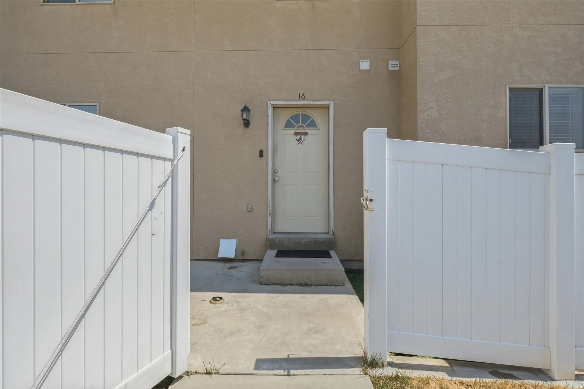 Cream-colored exterior, white entry door with arched window, exterior sconce lighting, concrete entryway, and white privacy fencing