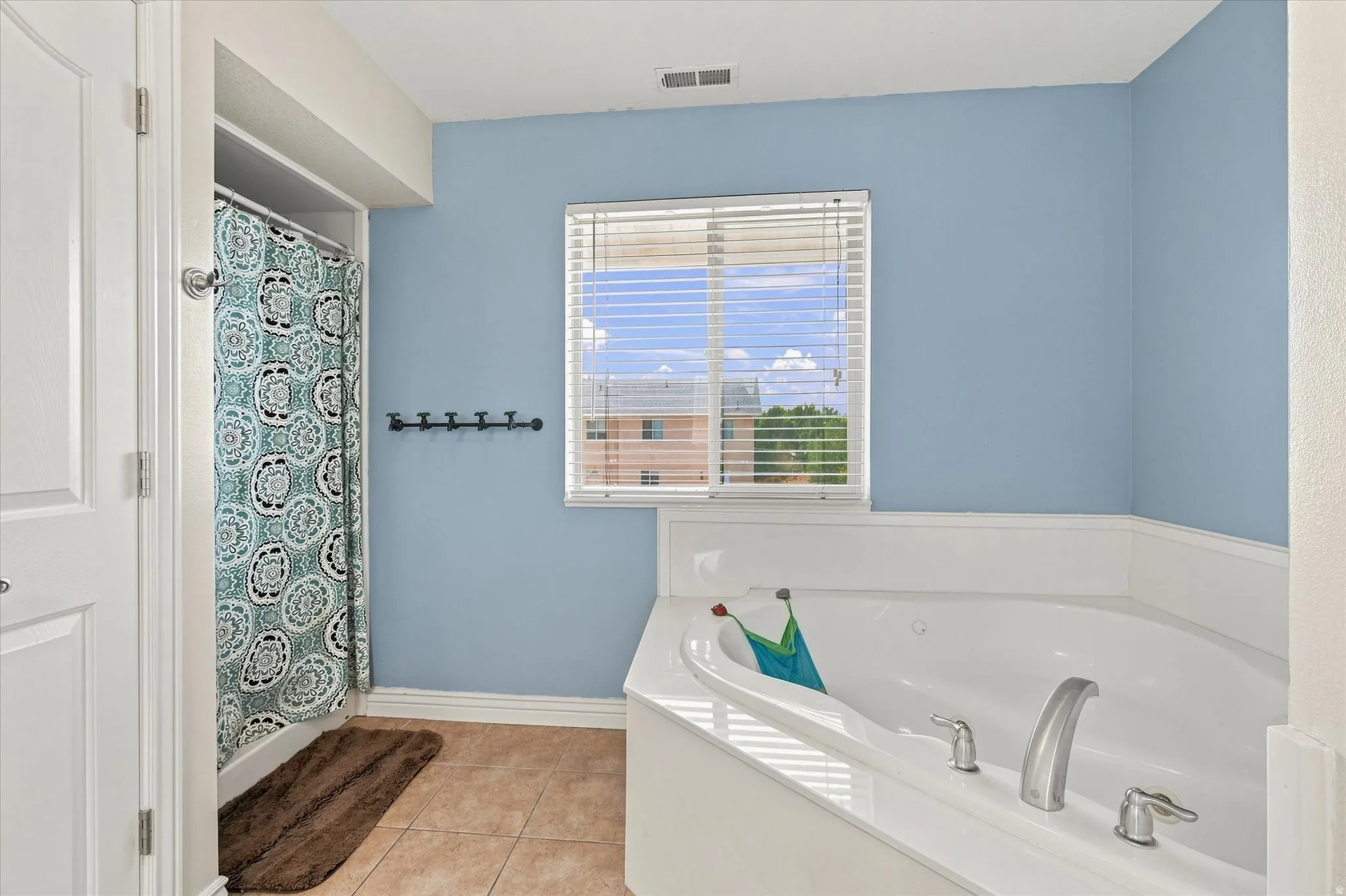 Built-in corner bathtub, tile flooring, window with blinds, and shower with shower curtain