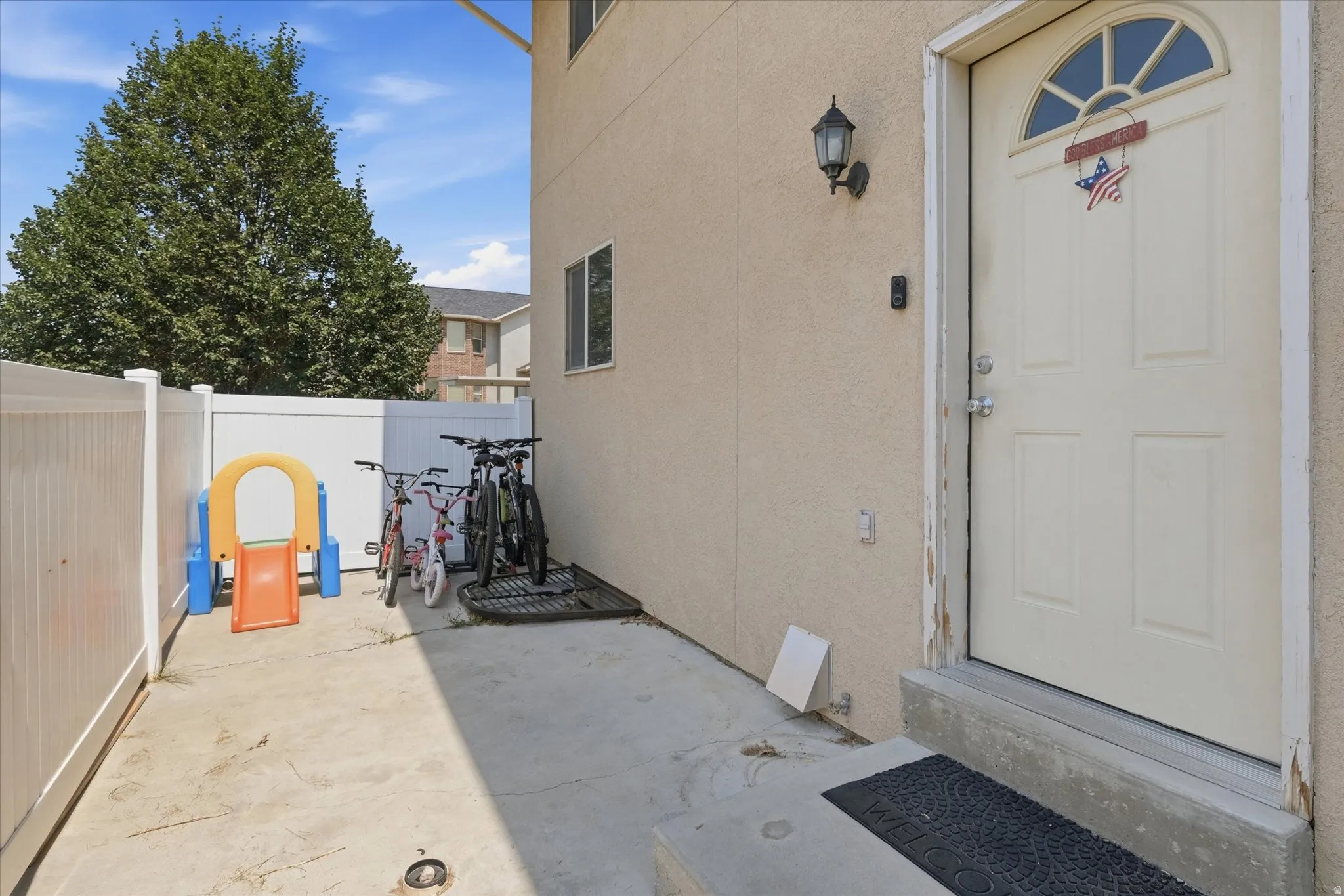 Exterior entry with a paneled door featuring an arched transom window, a wall-mounted light fixture, and a concrete pathway