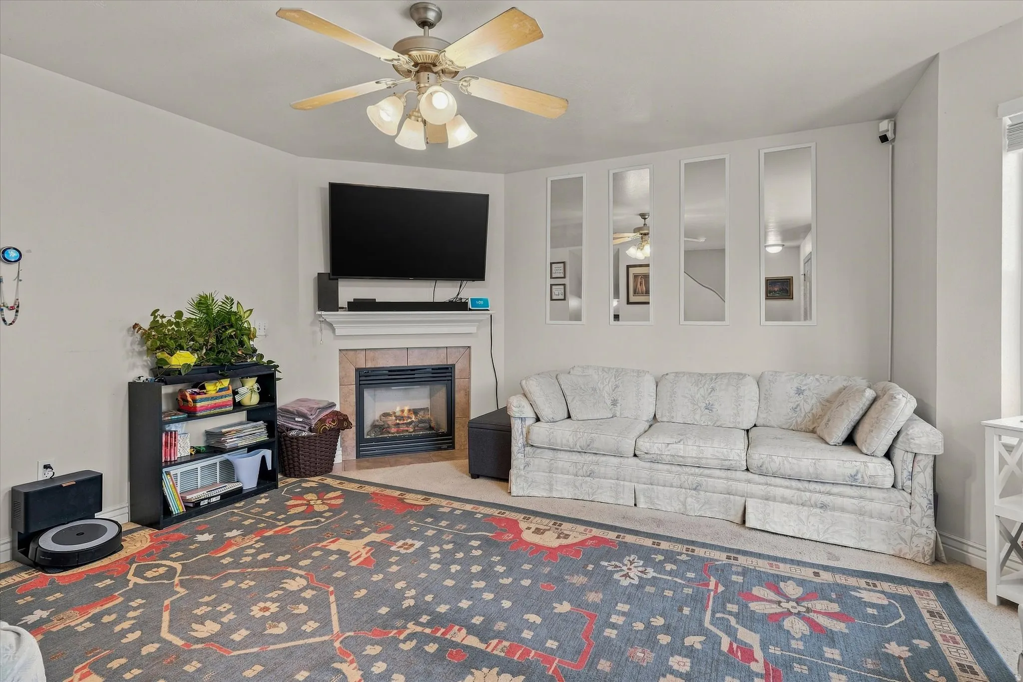 Living area featuring a ceiling fan, fireplace with a tile surround and mantel, and light-toned wall finishes