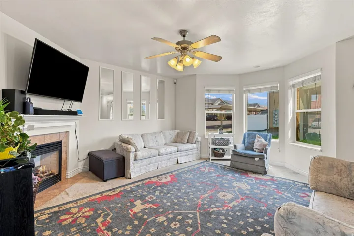 Fireplace with tile surround and mantel, ceiling fan with light fixture, bay windows, and carpet flooring