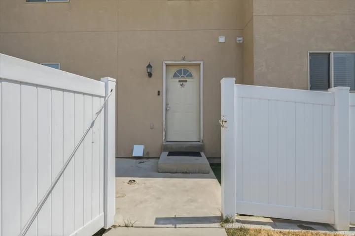 Cream-colored exterior, white entry door with arched window, exterior sconce lighting, concrete entryway, and white privacy fencing