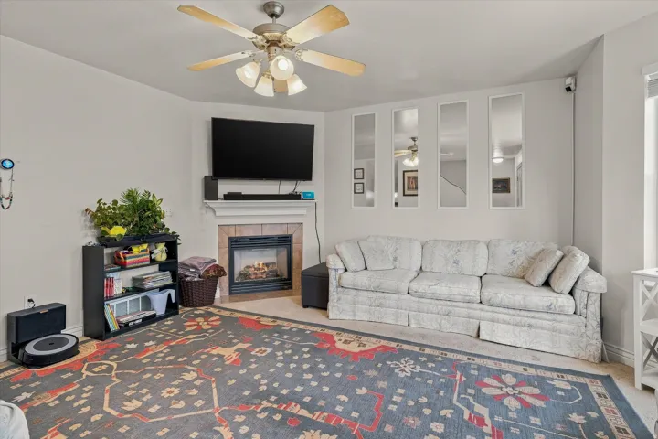 Living area featuring a ceiling fan, fireplace with a tile surround and mantel, and light-toned wall finishes