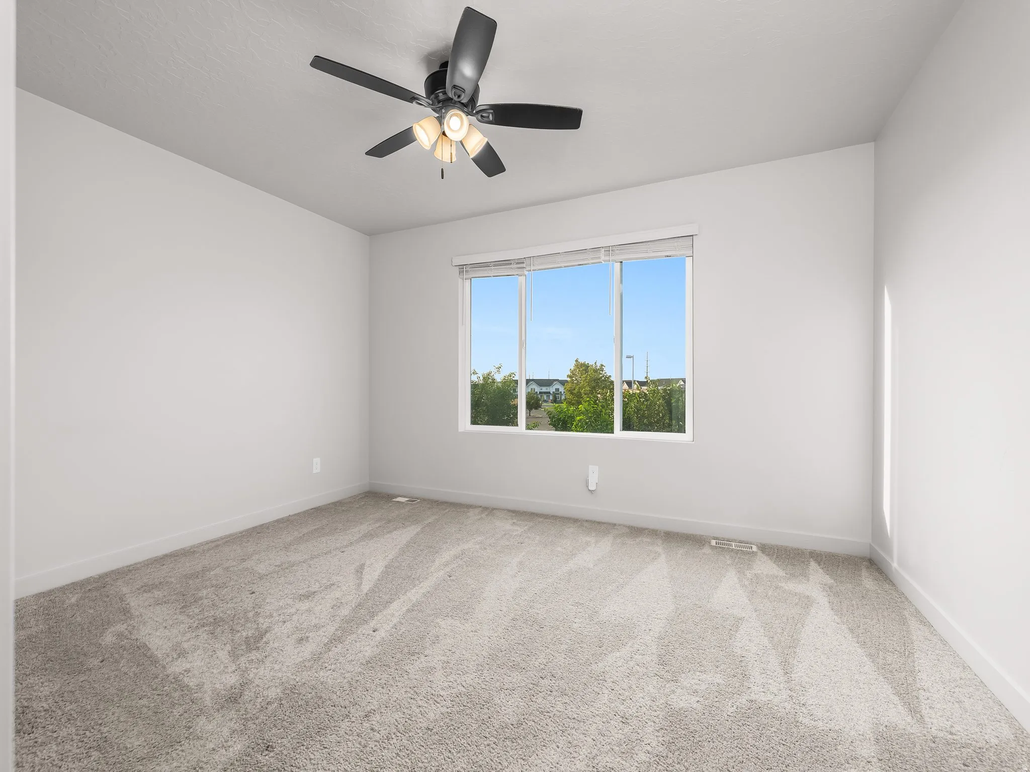 White walls, light-colored carpet, a large window, and a ceiling fan with integrated lighting