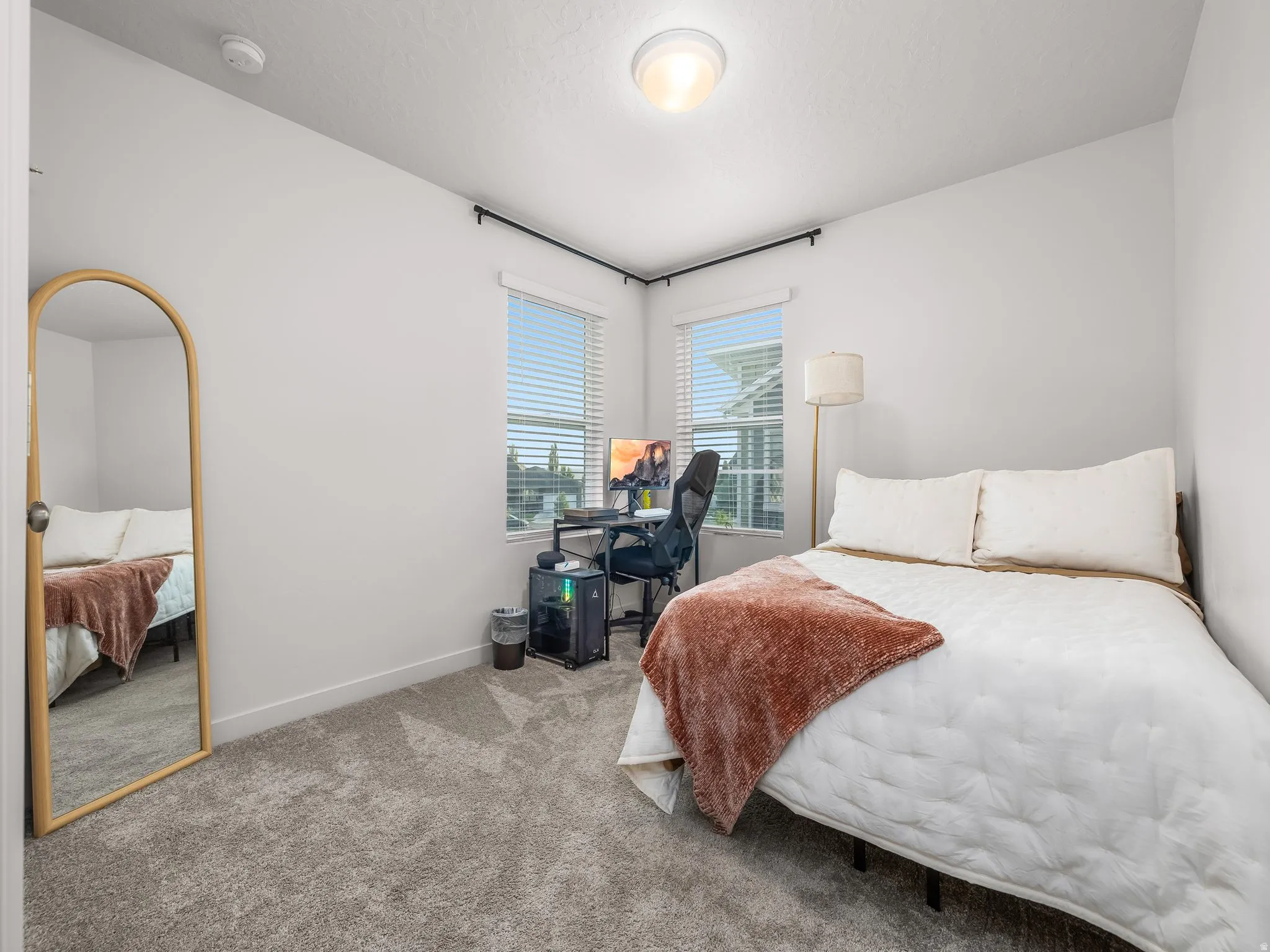 Recessed ceiling light, two windows with blinds, carpeted flooring, white walls, and a built-in desk area