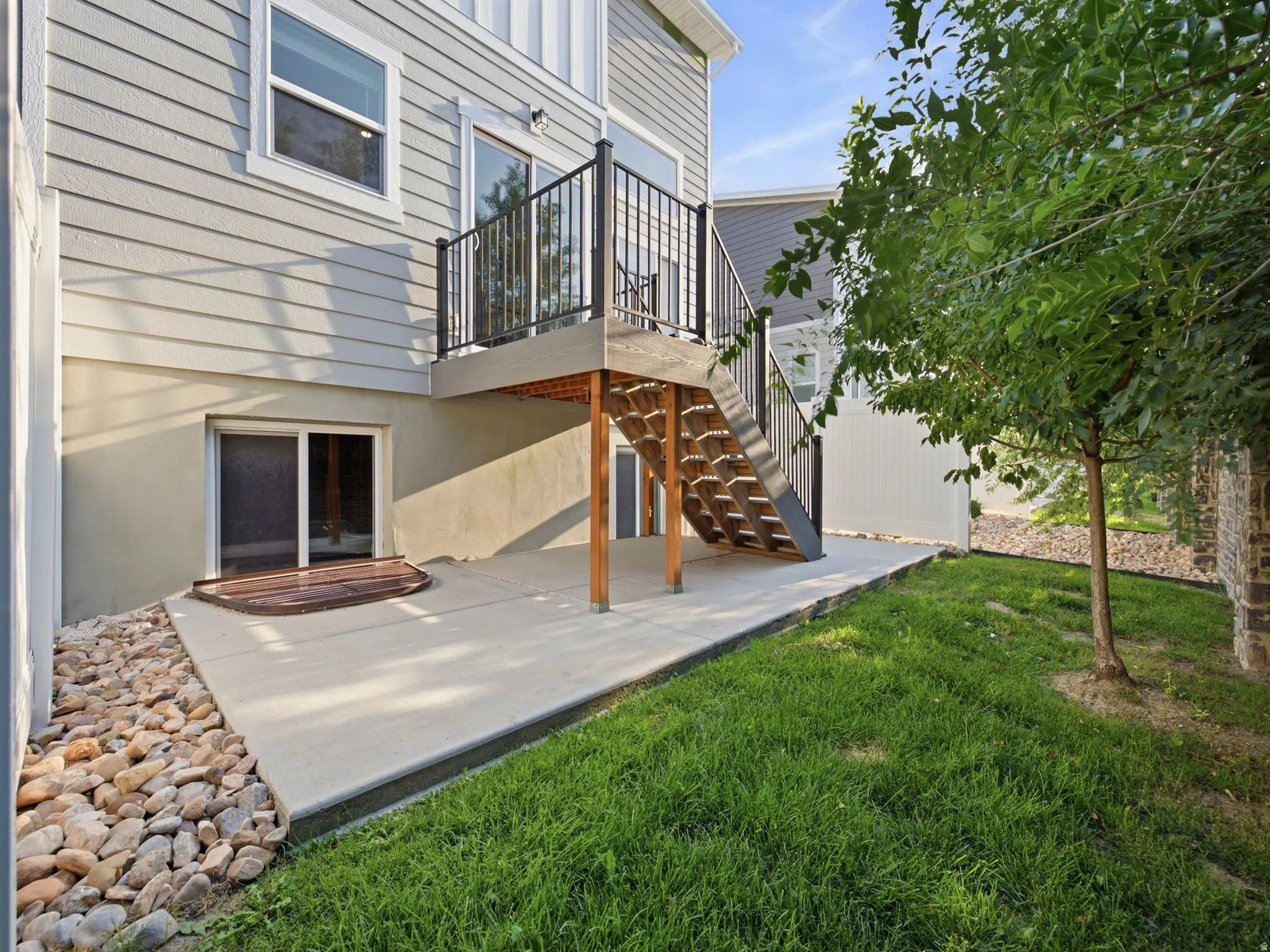 Rear exterior with light gray siding, concrete patio, and a deck featuring black railings and wood-finish stairs