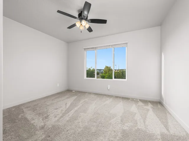 White walls, light-colored carpet, a large window, and a ceiling fan with integrated lighting