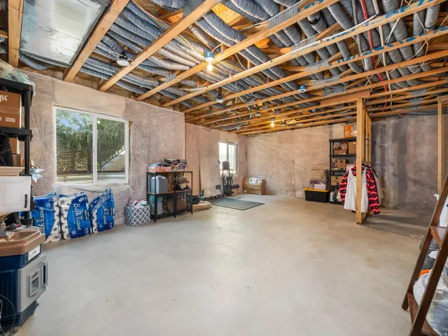 Expansive unfinished basement featuring an exposed wood joist ceiling, concrete flooring, and a large daylight window