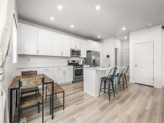 Kitchen featuring white cabinetry, stainless steel appliances, a center island with a sink, and wood-finish flooring