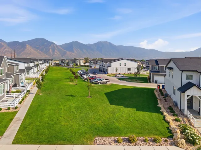 Community green space with mountain backdrop, residential properties featuring white and gray exteriors, and attached garages