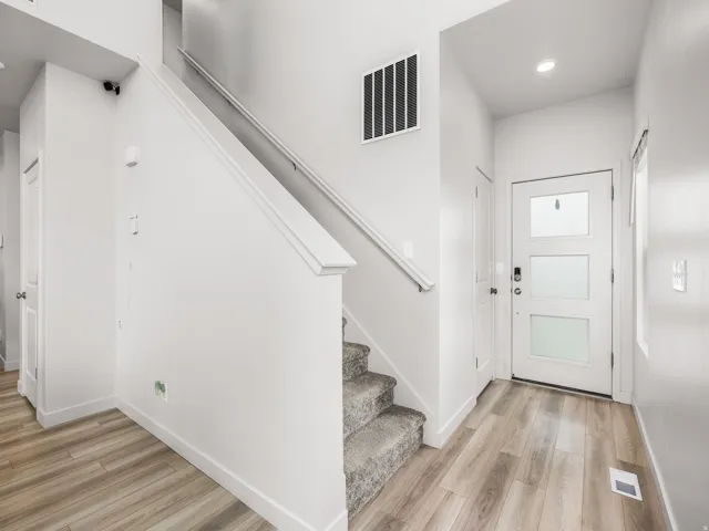Entryway featuring wood-finish flooring, a modern front door with frosted glass panels, and a carpeted staircase with a white handrail