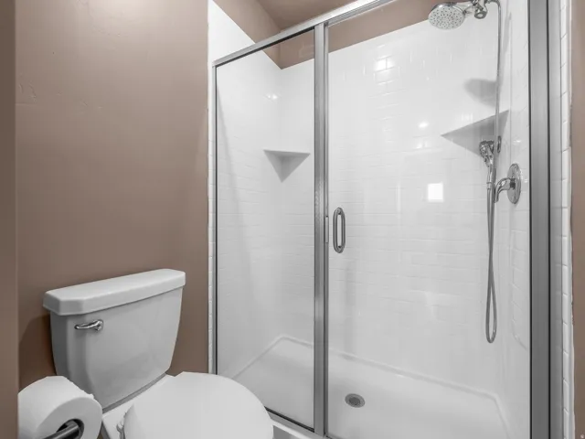 Glass-enclosed shower with white subway tile, integrated shelving, and a chrome shower head