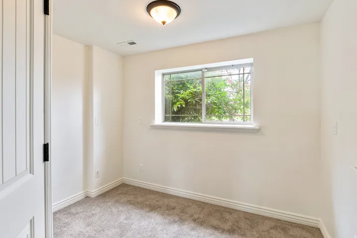 Carpeted room featuring a white paneled door, flush mount light fixture, and a window with exterior greenery
