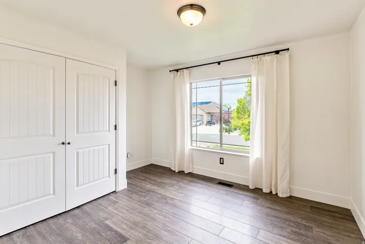Wood-finish flooring, white paneled double doors, window with white trim, and a semi-flush mount ceiling light fixture
