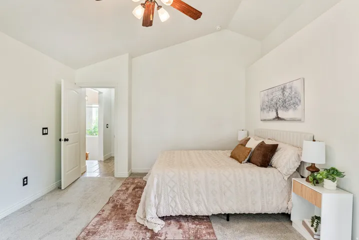 Vaulted ceiling, ceiling fan with light kit, neutral wall tones, carpet flooring, solid core door