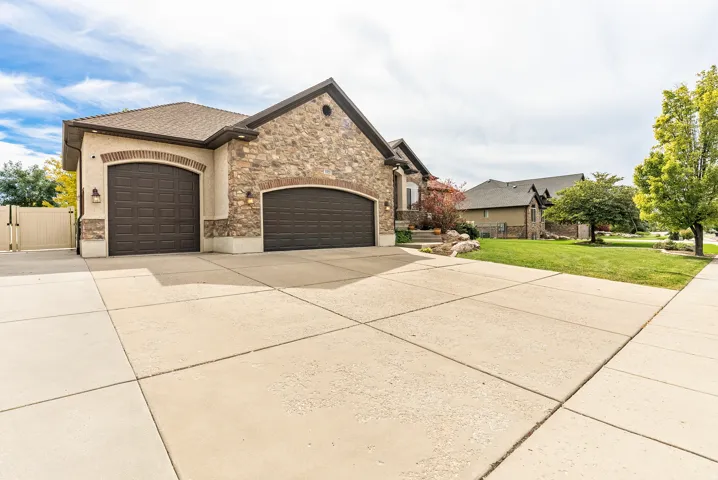 Stone and stucco exterior with two arched garage doors, a concrete driveway, and a manicured front lawn