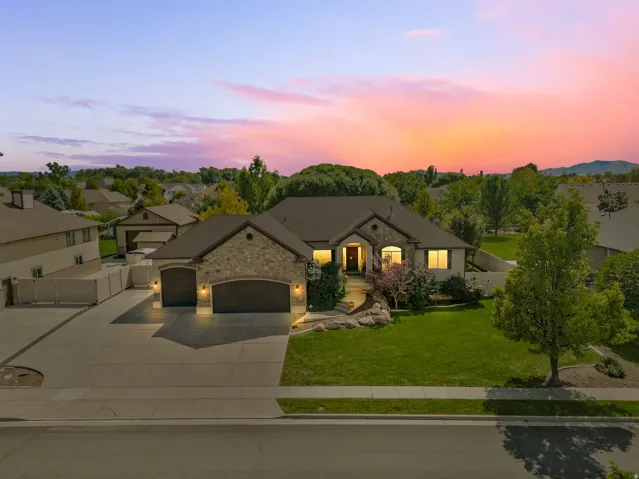 Stone and stucco exterior, arched garage doors, extensive paved driveway, established landscaping, and a manicured lawn
