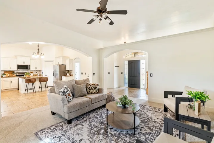 Arched doorways framing the kitchen and entryway, a ceiling fan with integrated lighting, a kitchen island with a built-in sink, and stainless steel appliances
