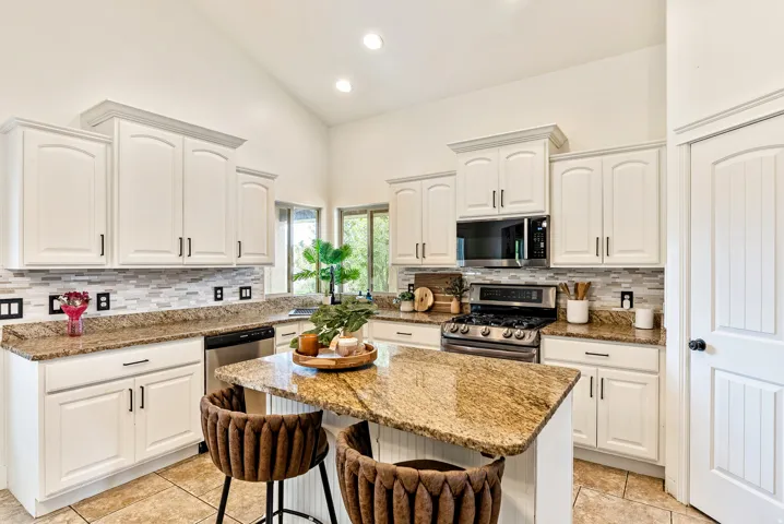 Kitchen featuring white cabinetry, granite countertops, a tiled backsplash, stainless steel appliances, and a central island