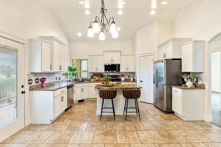Kitchen featuring vaulted ceilings, white cabinetry, a central island, stainless steel appliances, and tile flooring